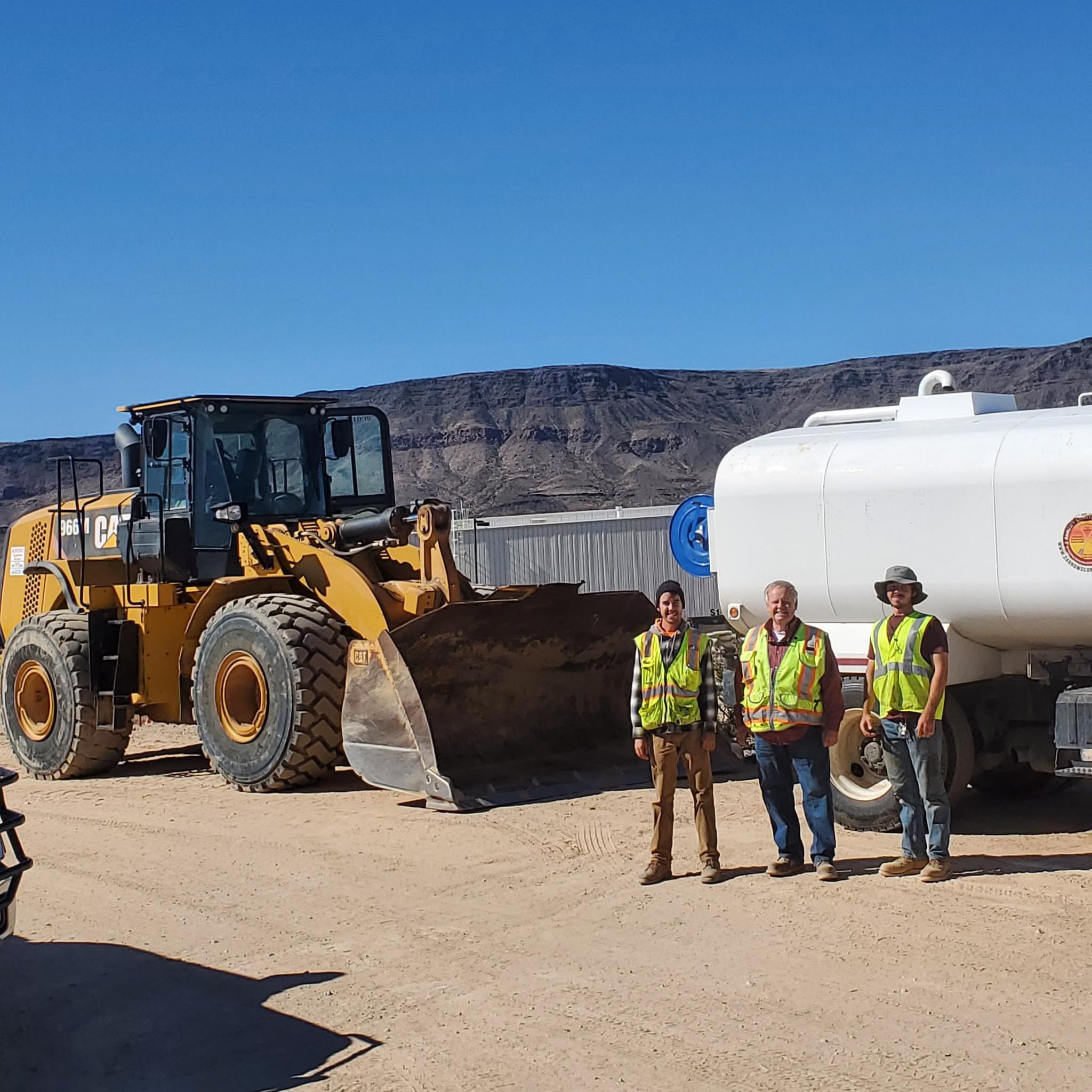 Group photo in front of water truck and loader